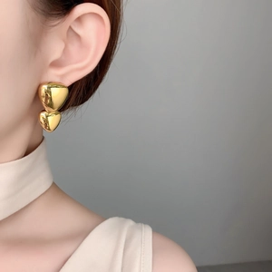 Close-up of heart-shaped 18K gold-plated mirror finish stud earrings worn by a model