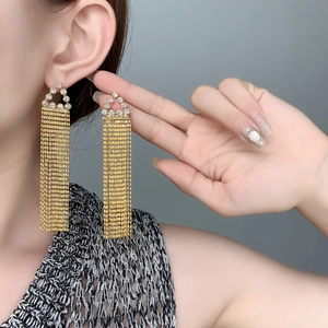 Vue détaillée de longues boucles d'oreilles à pompons dorés portées par un mannequin