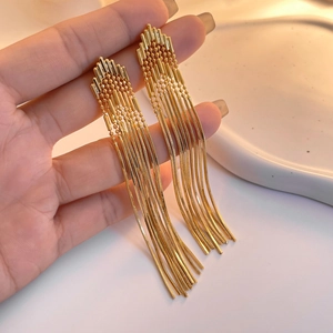 Detail of 18K gold plated long tassel chain earrings held in hand over ceramic tray