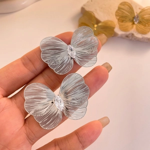 Macro shot of silver hollow butterfly earrings with marquise zircon on stone background