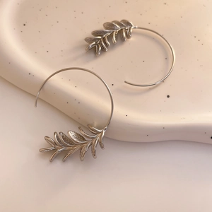 Detail of silver leaf-shaped hoop earrings on a textured ceramic dish for a vintage look