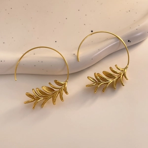 Macro detail of 18K gold plated leaf earrings on a ceramic display with elegant texture