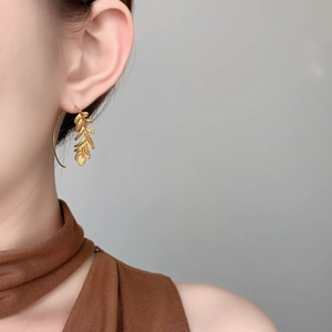 Detailed close-up of 18K gold-plated leaf drop earrings worn by a female model