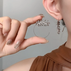 Detailed close-up of leaf-shaped silver earrings with intricate vein textures on model