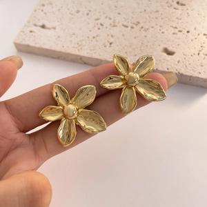 Detailed close-up of large 18K gold-plated flower studs held by a model for scale