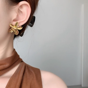 Close-up of 18K gold plated flower stud earring worn by a model in soft lighting