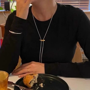 Minimalist gold bolo necklace and silver cuff bracelet worn over a black sweater