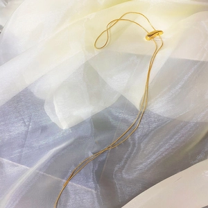 Close-up of golden sleek snake chain with adjustable sliding bead on soft fabric