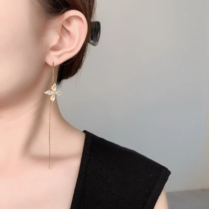 Detailed view of long gold tassel earrings with zircon four-leaf clover on model