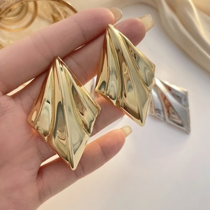 Detailed close-up of geometric diamond-shaped gold earrings with fine vertical textures