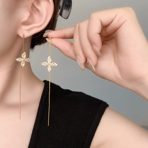 Close-up of a 18K gold plated long tassel earring with a zircon clover leaf on a model