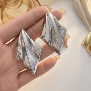 Close-up of silver geometric diamond-shaped earrings with unique folded metal texture