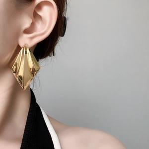 Detail of large gold geometric rhombus earrings with polished mirror origami finish