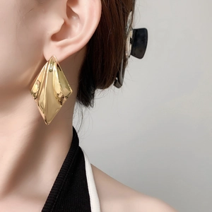 Modern geometric rhombus gold earrings with origami style textured surface on model