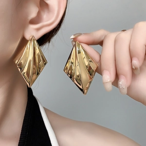 Close-up of oversized gold geometric earrings with elegant pleated metal texture on model