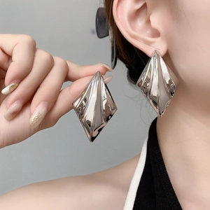 Macro detail of oversized silver-tone geometric rhombus earrings with mirror finish texture