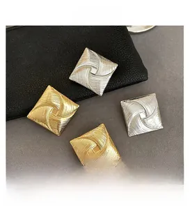 Macro view of square gold and silver earrings with radial windmill texture on leather