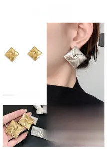 Detailed view of square stud earrings with spiral texture in gold and silver finish