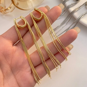 Close-up of gold U-shaped earrings with delicate long snake chain tassels held by hand