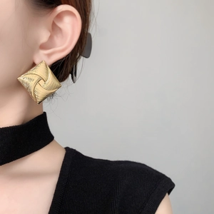 Detailed close-up of gold square stud earrings featuring a 3D windmill texture pattern