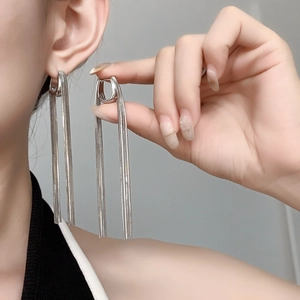 Detail of silver long chain tassel earrings with U-shaped clasp worn by a model