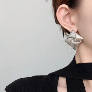 Detailed view of square stud earrings with radial texture on a model wearing black