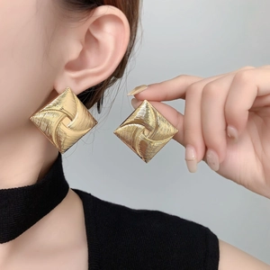 Macro detail of large square gold earrings with radial spiral texture on model