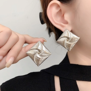 Macro detail of square silver stud earrings featuring a unique spiral windmill texture