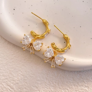 Macro shot of gold-plated bow earrings featuring faceted crystals on a ceramic dish