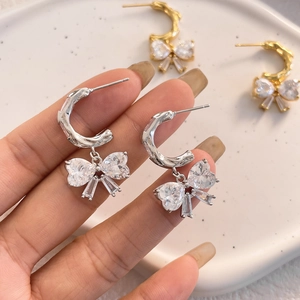 Sparkling blue crystal bow drop earrings in silver and gold displayed on a ceramic tray