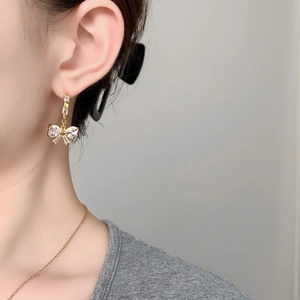 Close-up of golden bow earrings with sparkling crystals worn on ear for elegant style