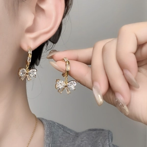 Close-up of gold butterfly earrings with blue crystals and stones worn on ear