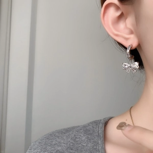 Detailed view of model wearing a silver bow earring with shimmering blue crystal accents