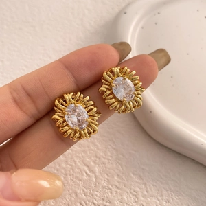 Close-up of gold flower stud earring featuring an oval zircon center and textured metal