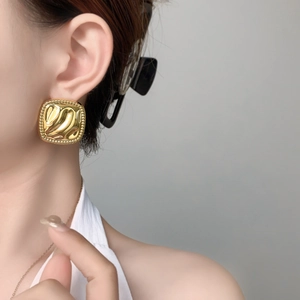 Detail of square gold-plated earrings with embossed wave texture and beaded edges