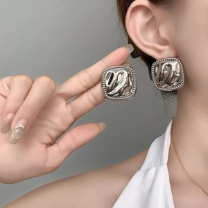 Detailed view of silver square stud earrings with irregular hammered texture and bead edges
