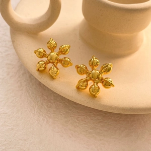 Détail de boucles d'oreilles flocons dorés avec perles centrales sur plat en céramique