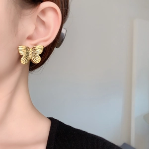 Detailansicht der 18K vergoldeten Schmetterlings-Ohrstecker mit Vintage-Textur am Modell