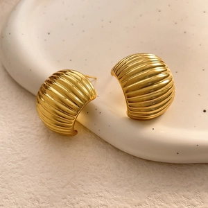 Macro detail of gold C-shaped ribbed earrings with elegant metallic texture finish