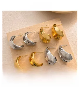 Détails de boucles d'oreilles créoles texturées en argent, or et bronze sur travertin