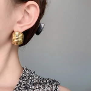Close-up of chunky gold C-shaped earrings with ripple texture on female model's ear