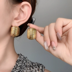 Close-up of chunky gold C-shaped earrings with textured horizontal ridges on model ear