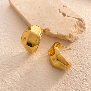 Détail macro de boucles d'oreilles dorées géométriques brillantes sur socle pierre