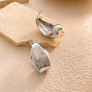 Détail de boucles d'oreilles argentées effet miroir sur un présentoir en pierre