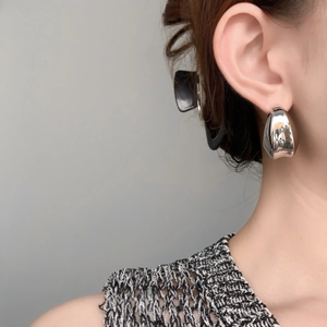 Gros plan de créoles demi-lune en argent poli portées par un mannequin au style épuré