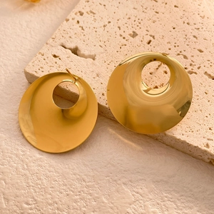 Macro detail of high-polish gold hollow disc earrings on a beige travertine stone