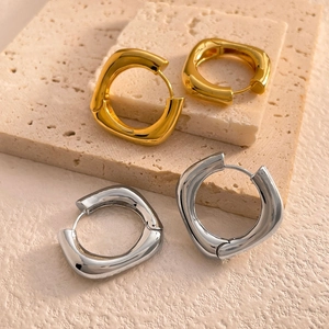 Détail de boucles d'oreilles géométriques dorées et argentées sur un plateau en pierre