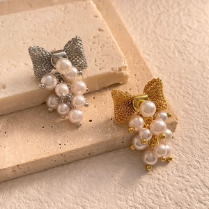 Detailed close-up of gold and silver bow stud earrings with clusters of lustrous pearls