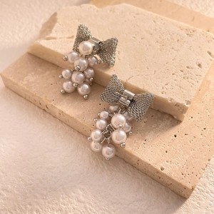 Detailed shot of silver bow stud earrings with clustered pearls on a stone base