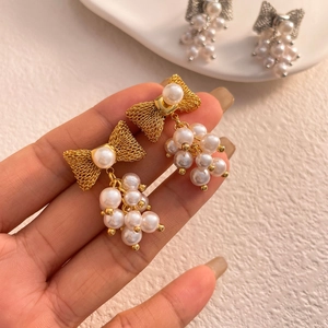 Detailed shot of bow-shaped gold earrings with cluster pearl drop charms for women